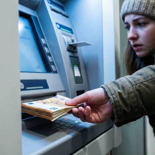 Eine Hand zieht hastig ein dickes Bündel Geldscheine aus dem Ausgabeschacht eines Geldautomaten.