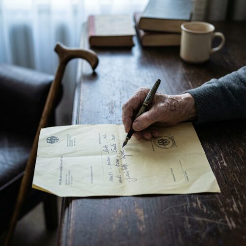 Nahaufnahme einer zittrigen Hand, die eine kaum leserliche handschriftliche Änderung auf ein formelles Dokument kritzelt.