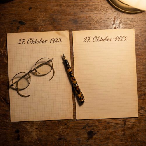 Kariertes und liniertes Papier mit identischem handschriftlichem Datum neben einem Füller auf dunklem Holztisch.
