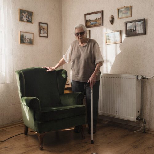 Eine sehbehinderte Frau mit dunkler Brille tastet in ihrem Wohnzimmer unsicher nach der Lehne eines Sessels.