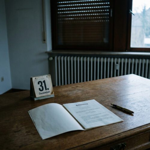 Ein aufgeschlagener Kalender mit dem 31. Dezember liegt still neben einem Erbvertrag auf einem Schreibtisch.